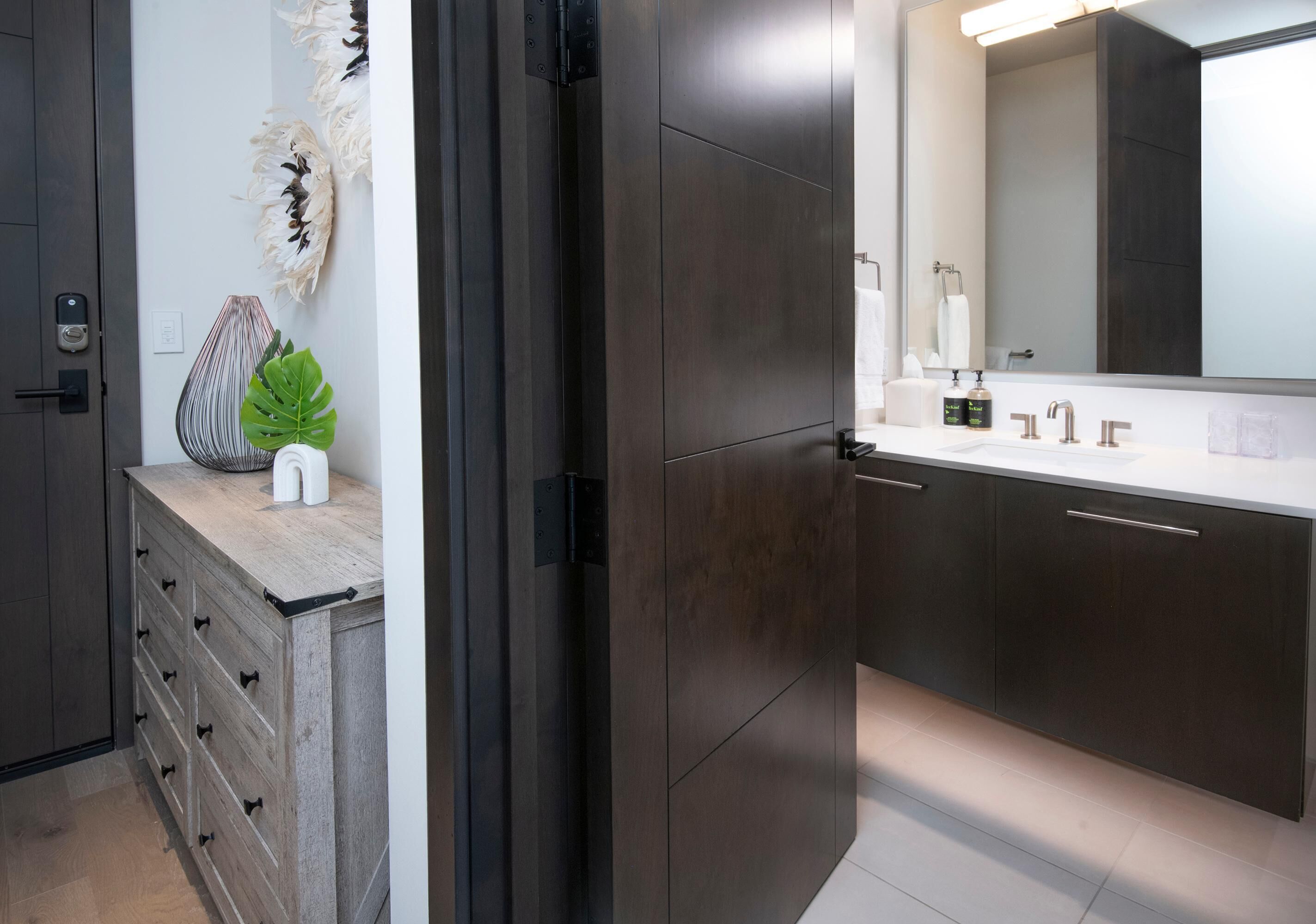 A modern bathroom with a dark wood vanity, a white sink, and a large mirror.
