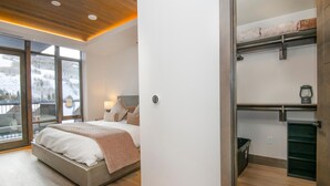 A bedroom with a bed, a nightstand, a lamp, a window with a view of a snowy landscape, and a sliding door leading to a balcony. - Altus 305, 3BD Vail Village Condo With Views (Vail)