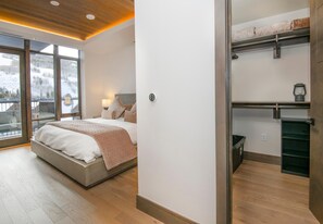 A bedroom with a bed, a nightstand, a lamp, a window with a view of a snowy landscape, and a sliding door leading to a balcony. - Altus 305, 3BD Vail Village Condo With Views (Vail)