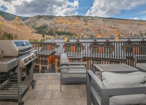 Ein Balkon mit Grill, Sitzgelegenheit im Freien und Blick auf eine Berglandschaft.