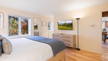 Een slaapkamer met een bed, een kaptafel, een nachtkastje, een lamp en een raam met uitzicht op bomen.