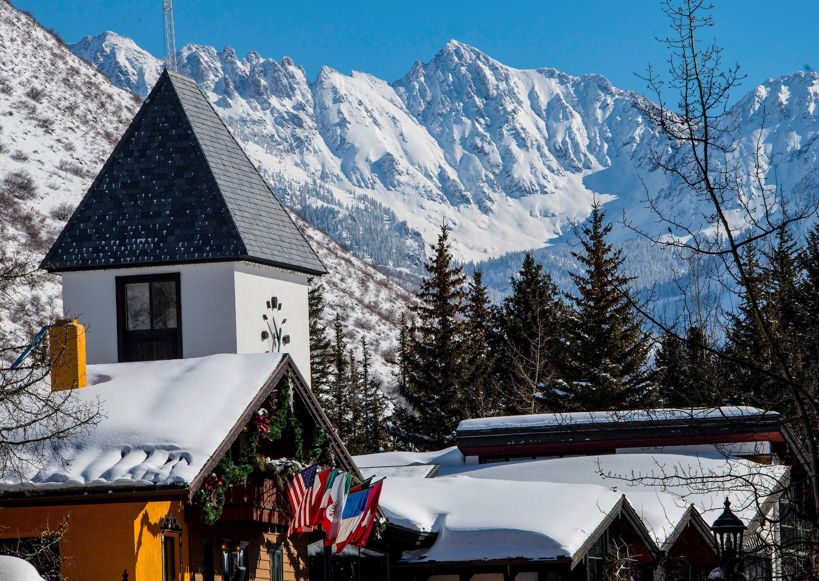 A snow-covered mountain village with a church, flags, and traditional buildings.