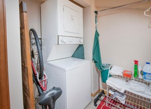 Ein Waschbereich mit Waschmaschine, Wäscheständer und verschiedenen Reinigungsmitteln.