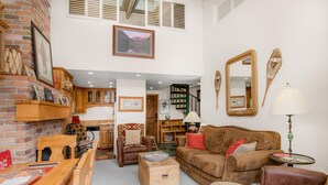 Een gezellige woonkamer met een open haard, houten meubels, een trap en een grote spiegel.