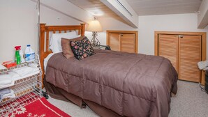Een slaapkamer met een houten bed, een rood-wit kleed, een metalen droogrek en twee houten kasten.