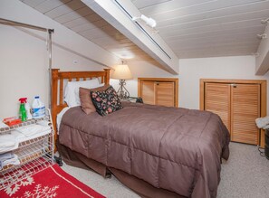 Ein Schlafzimmer mit einem Holzbett, einem roten und weißen Teppich, einem Wäscheständer aus Metall und zwei Holfächern.