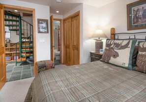 A bedroom with a plaid bedspread, a wooden staircase, a wooden wardrobe, a framed picture on the wall, and a lamp on a bedside table. - Wall Street 305, 1BD + Loft Condo in Vail Village (Vail)