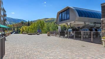 Un espacio al aire libre pavimentado con una parada de autobús techada, montañas al fondo y un edificio con un cartel que dice 'Riverfront Express'.