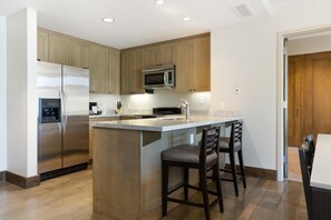 A modern kitchen with a stainless steel refrigerator, a microwave, and a built-in oven. There is a large island with bar stools. - Riverfront Resort & Spa 421, 2BD Condo With Mtn Views (Avon)