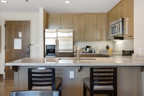 A modern kitchen with wooden cabinets, stainless steel appliances, and a marble countertop. - Riverfront Resort & Spa 421, 2BD Condo With Mtn Views (Avon)