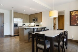 A modern kitchen with a central island, built-in appliances, and a dining area with a large table and chairs. - Riverfront Resort & Spa 421, 2BD Condo With Mtn Views (Avon)