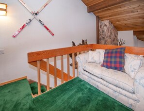 Ein Zimmer mit einer Holztreppe, einem Sofa mit gemusterten Kissen und einem an der Wand befestigten Skiständer.