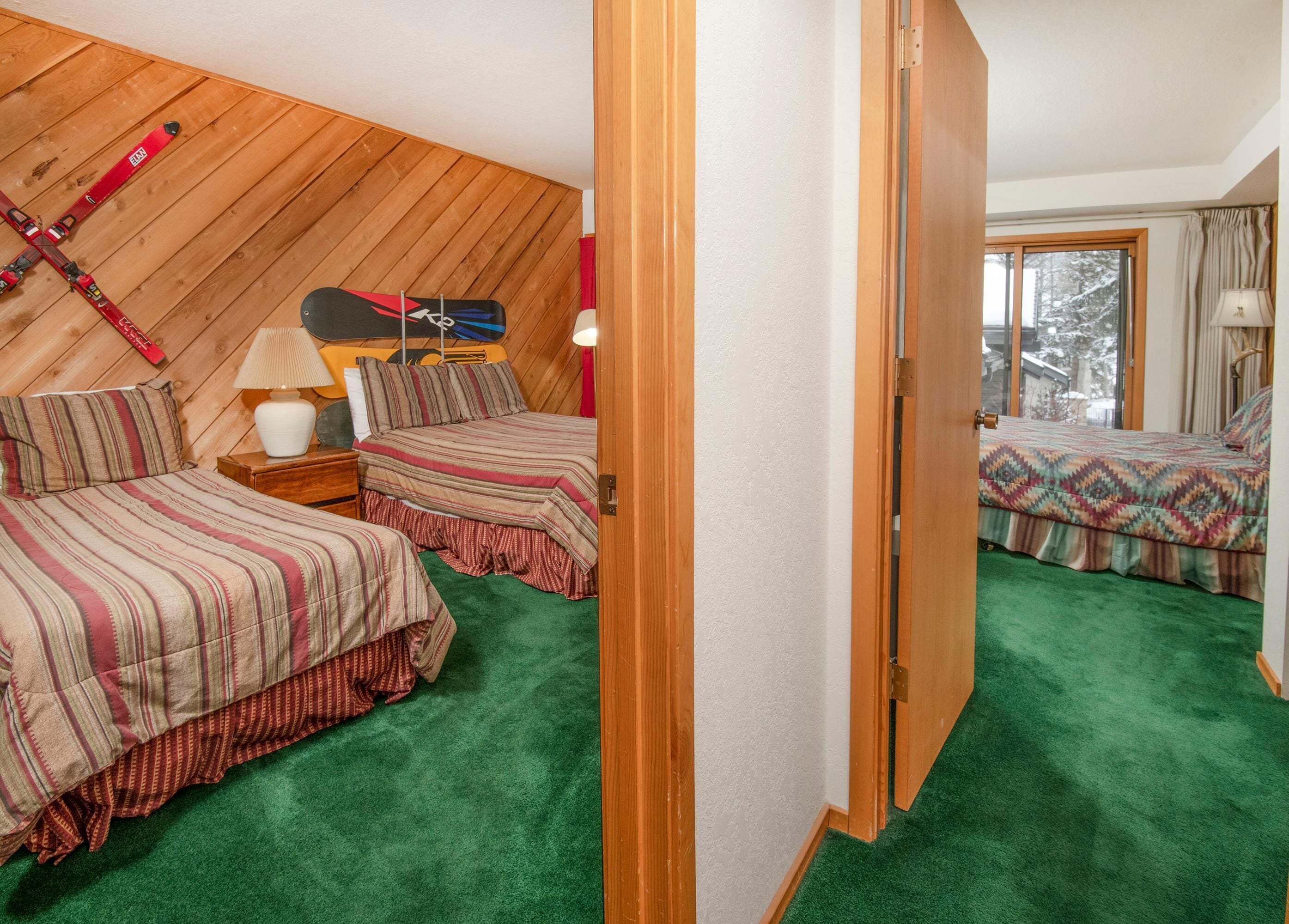 A room with two beds, a wooden sloped ceiling, a window with a view, and a door.