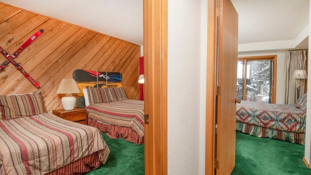 A room with two beds, a wooden sloped ceiling, a window with a view, and a door. - Ridgepoint 187, 3BD Townhome in Beaver Creek (Avon)