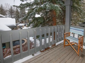 Eine Holzterrasse mit einer Bank, schneebedeckten Bäumen und einem Haus im Hintergrund.