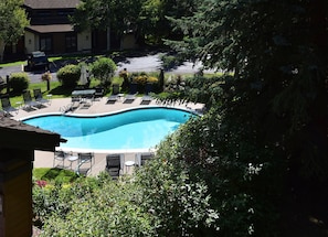 Ein Swimmingpool mit Liegestühlen und einer überdachten Liegefläche, umgeben von Grünflächen, mit einem Wohngebäude im Hintergrund.