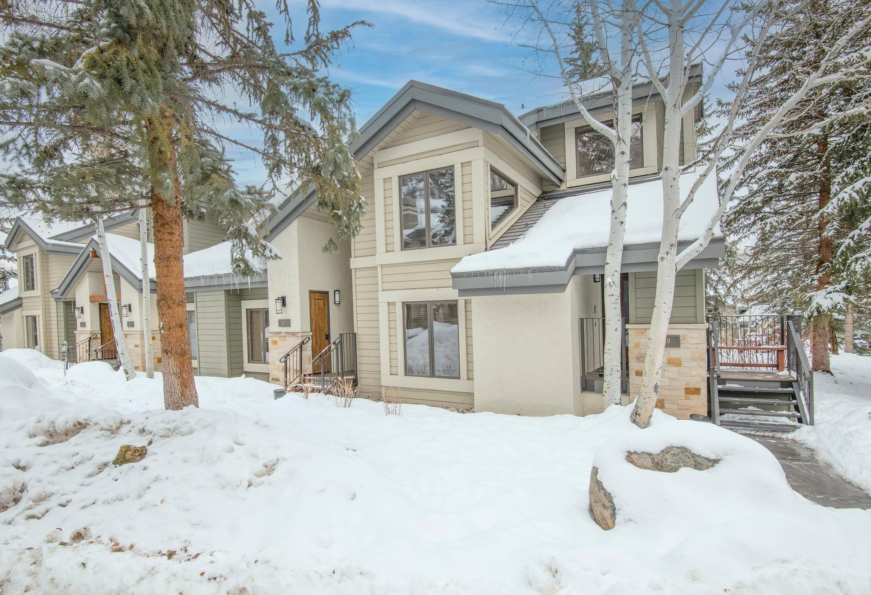 A residential building with a snow-covered roof, a visible staircase, and a sign indicating a property for sale.