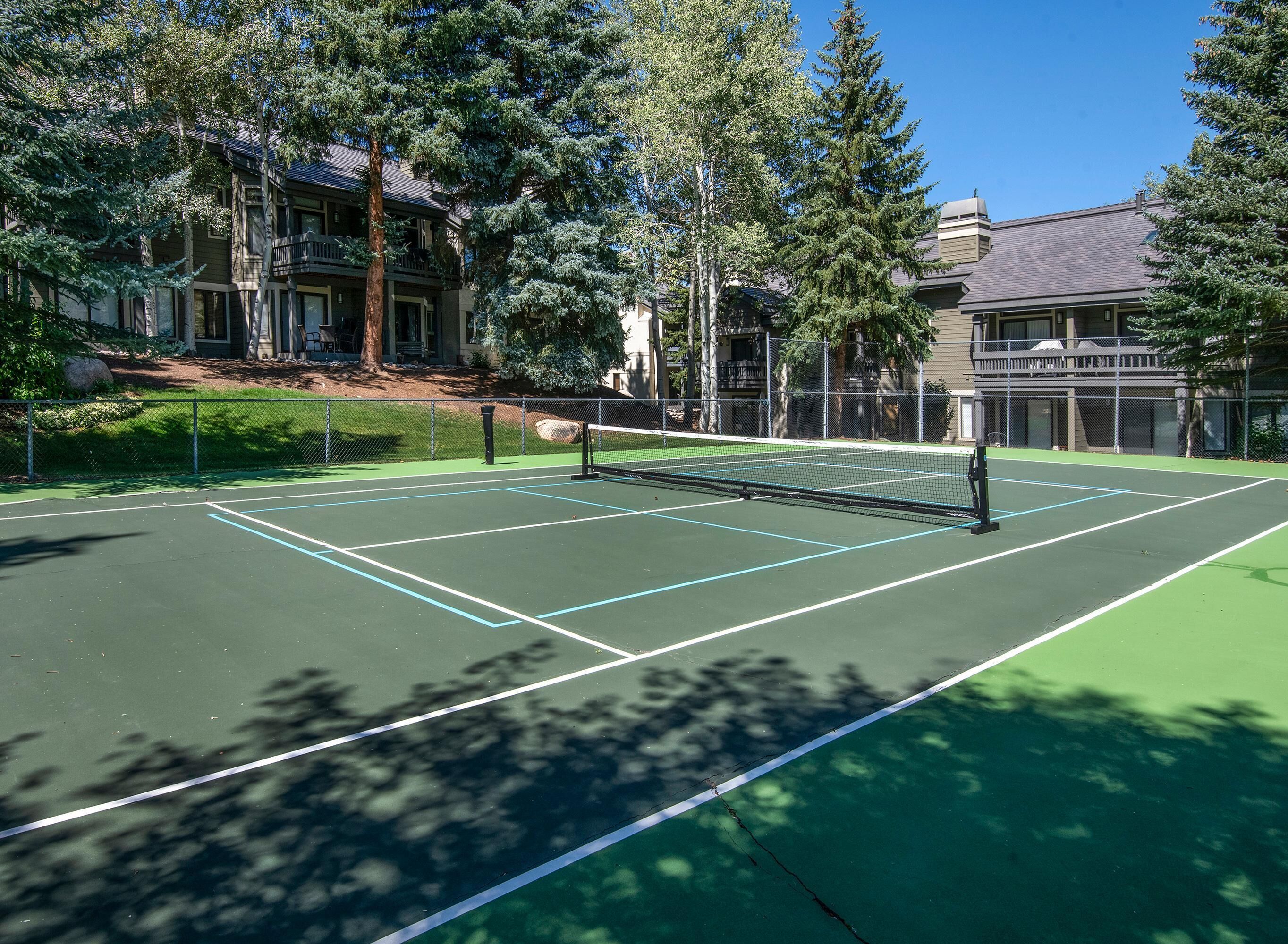 A tennis court surrounded by trees and buildings.