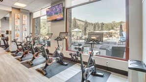 Ein Fitnessraum mit Ergometer, einem Bildschirm und Blick auf einen Poolbereich.