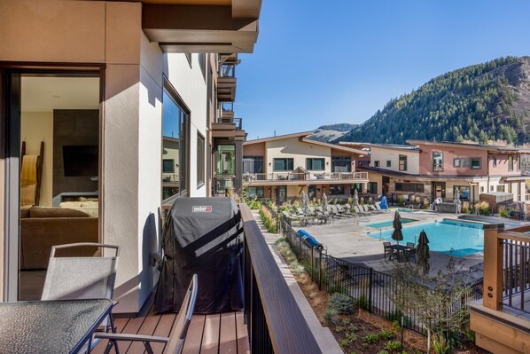 Un balcón con parrilla, una zona de piscina con sillones de descanso y montañas al fondo.