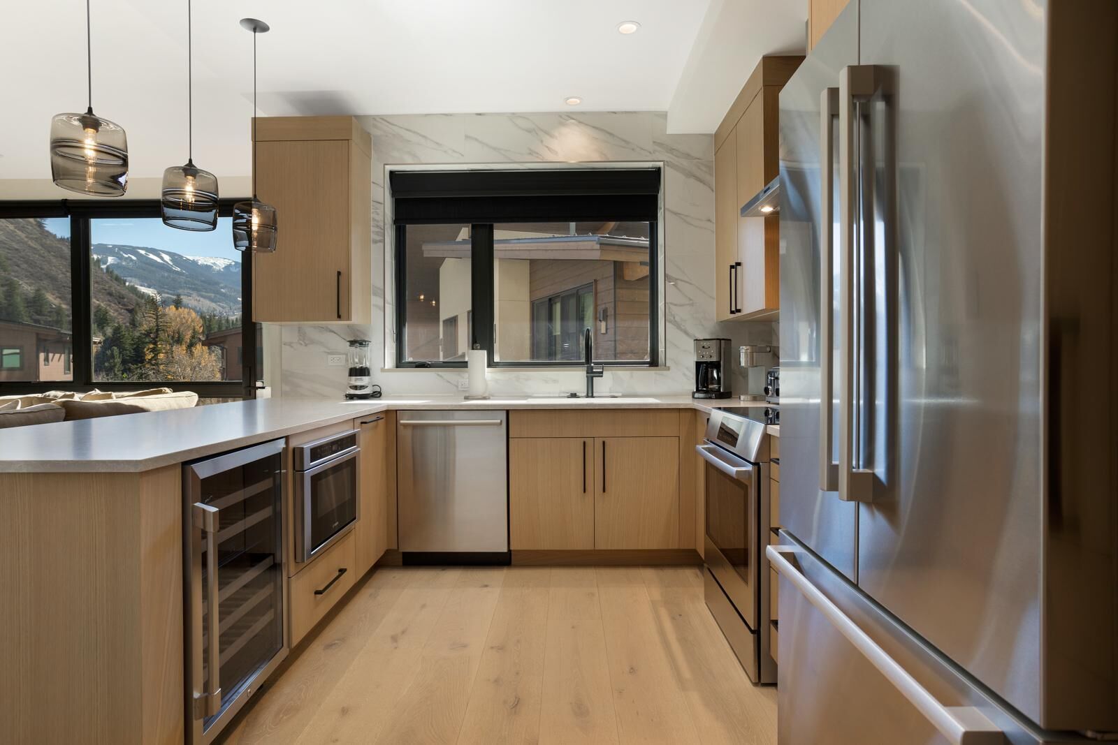Una cocina moderna con armarios de madera, electrodomésticos de acero inoxidable y un amplio ventanal con vistas a la montaña.