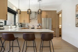 A modern kitchen with a large island, stainless steel appliances, and pendant lighting. - One Riverfront 106, 2BD Townhome With Beaver Creek Views (Avon)