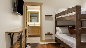 Ein Zimmer mit einem Etagenbett, einem Holztisch, einem Spiegel und einem Badezimmer mit Waschbecken und Spiegel.