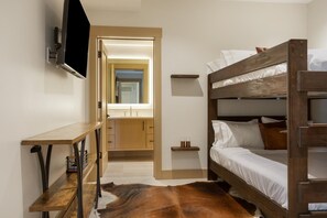 A room with a bunk bed, a wooden desk, a mirror, and a bathroom with a sink and mirror. - One Riverfront 106, 2BD Townhome With Beaver Creek Views (Avon)