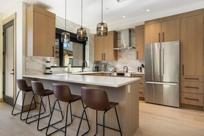 A modern kitchen with a marble countertop, stainless steel appliances, and wooden cabinets. - One Riverfront 106, 2BD Townhome With Beaver Creek Views (Avon)