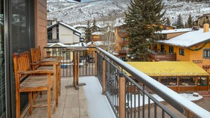 A balcony with wooden chairs, a yellow awning, and a view of snow-covered buildings and mountains. - Wall Street 302, 1BD + Loft Condo in Vail Village (Vail)