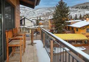 Un balcon avec des chaises en bois, un auvent jaune et une vue sur des bâtiments et des montagnes enneigés.