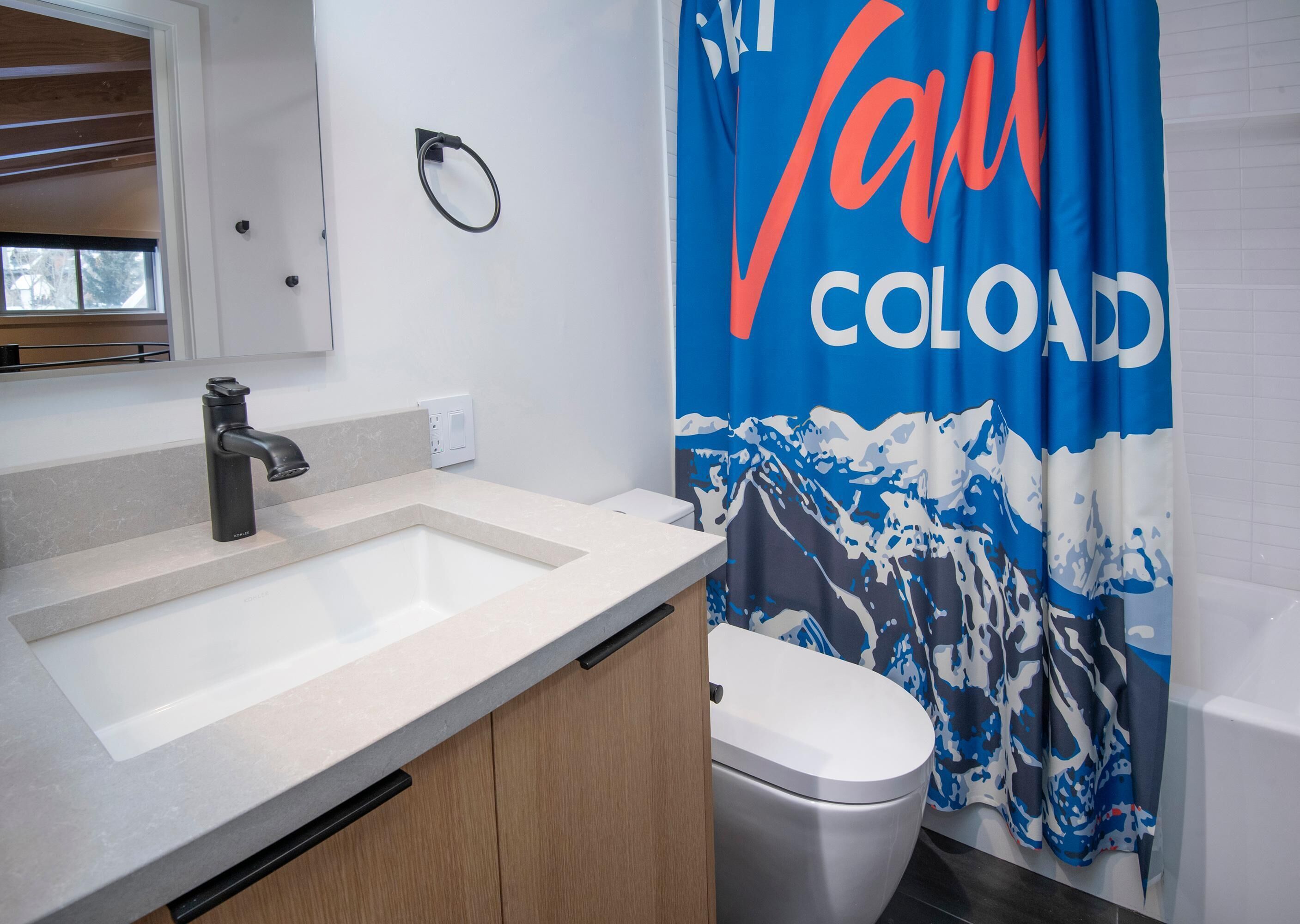 Ein Badezimmer mit einem modernen Waschbecken, WC und einer Duschvorhang mit Bergmotiv.