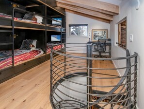 Un lit superposé avec un téléviseur, un bureau avec une chaise et un escalier en colimaçon.