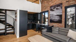 A modern interior with a staircase, kitchen, dining area, and a sofa with a view of a snowy mountain. - Wall Street 302, 1BD + Loft Condo in Vail Village (Vail)