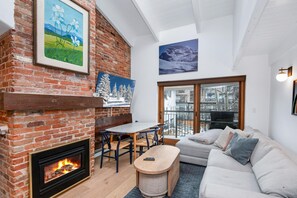 A living room with a fireplace, a sofa, a dining table, and artwork on the walls. - Wall Street 307, 1BD + Loft Condo in Vail Village (Vail)