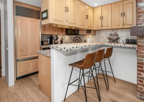 A kitchen with wooden cabinets, a microwave, a toaster, and a brick wall. - Wall Street 307, 1BD + Loft Condo in Vail Village (Vail)