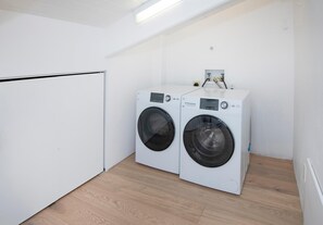 A laundry room with two white front-loading washing machines, a white door, and a wooden floor. - Wall Street 307, 1BD + Loft Condo in Vail Village (Vail)