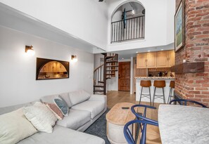 A spacious living area with a sofa, a coffee table, and a dining area with chairs. A staircase leads to an upper level with a balcony. - Wall Street 307, 1BD + Loft Condo in Vail Village (Vail)