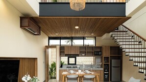 A modern interior with a dining area, kitchen, and living space, featuring a staircase and large windows. - Bintang Villas Ubud (Ubud)