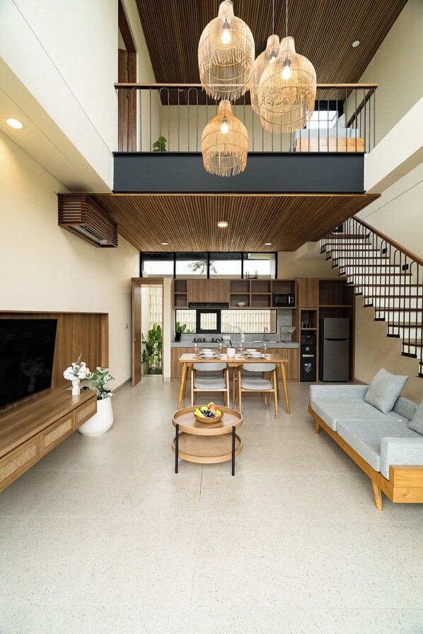 Un interior moderno con comedor, cocina y sala de estar, que incluye una escalera y ventanas amplias.