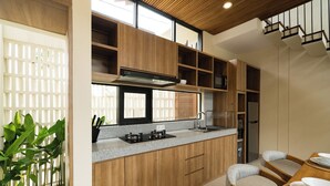 A modern kitchen with wooden cabinets, a gas stove, and a dining area with a table and chairs. - Bintang Villas Ubud (Ubud)