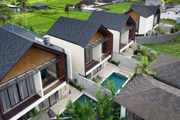 Um resort moderno com várias villas, uma piscina e vegetação exuberante.
