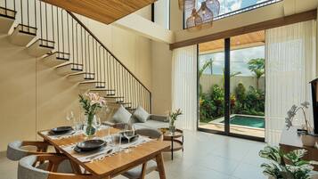 A modern interior with a wooden staircase, a dining area with a table set for two, and a view of a swimming pool through large glass doors.