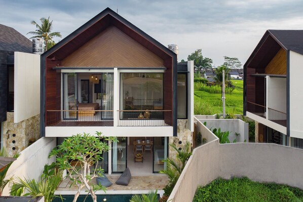 Ein modernes, zweistöckiges Haus mit Balkon, Schwimmbad und üppiger Bepflanzung.