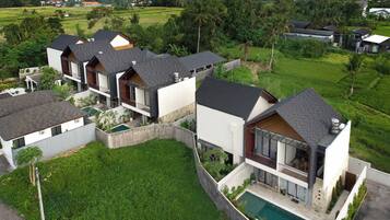 A modern multi-story residential building with a swimming pool, surrounded by lush greenery and fields.