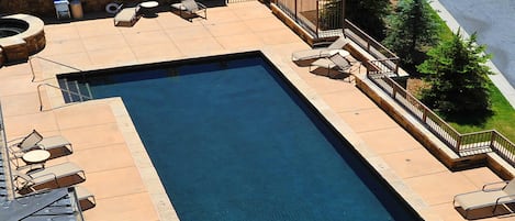 Una piscina rectangular con sillas de descanso y un muro de piedra.