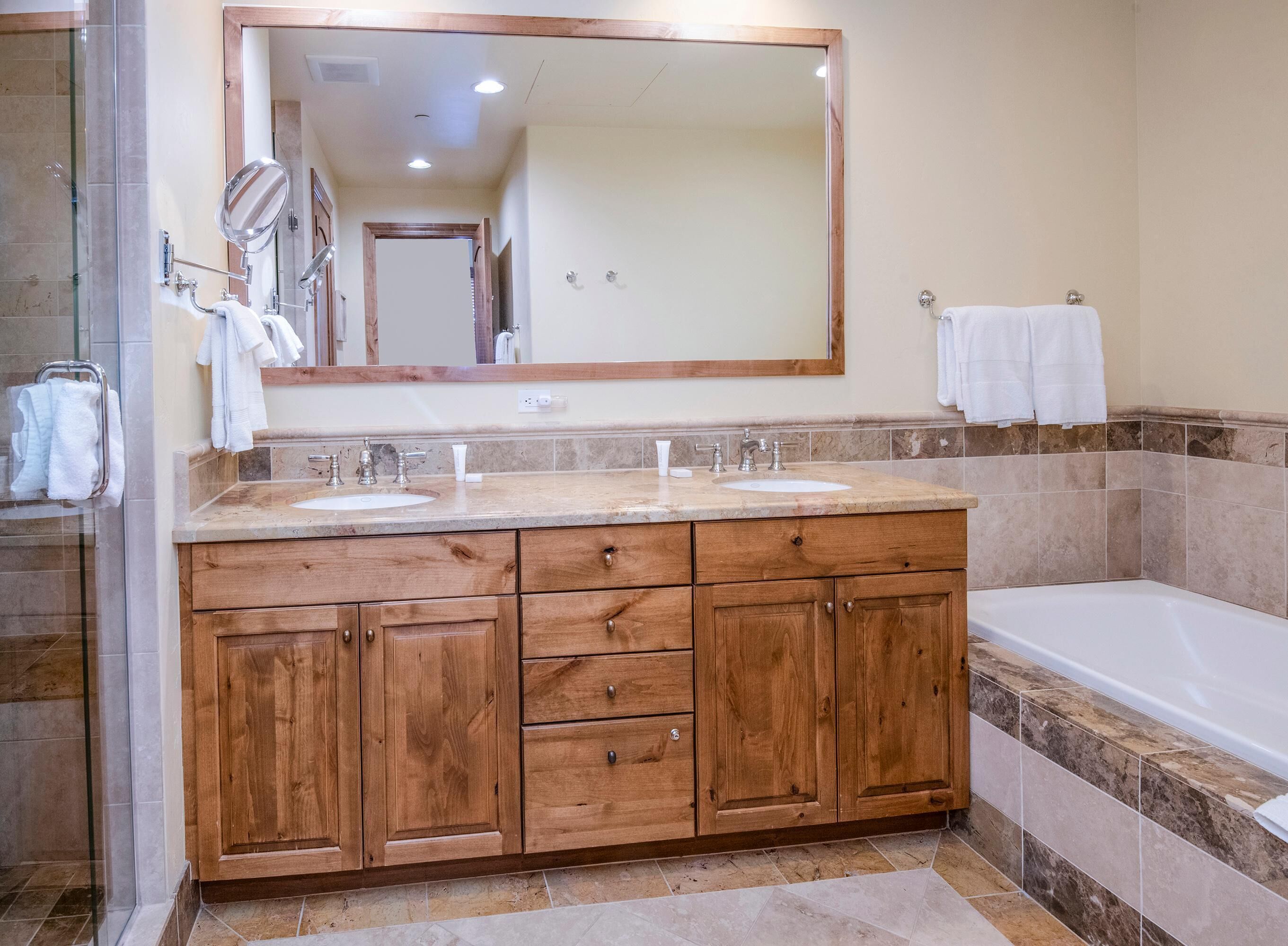 A bathroom with a wooden vanity, two sinks, a large mirror, and a bathtub.