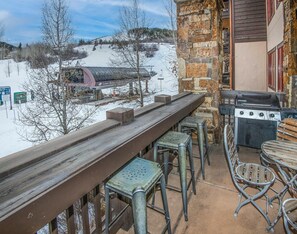 Eine Terrasse mit Steinmauer, Grill und Blick auf eine Seilbahn.