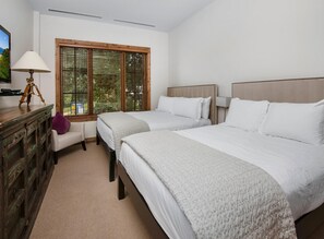 Ein Hotelzimmer mit zwei Betten, einem Holzschrank, einem Schreibtisch mit Lampe und einem Fenster mit Jalousien.