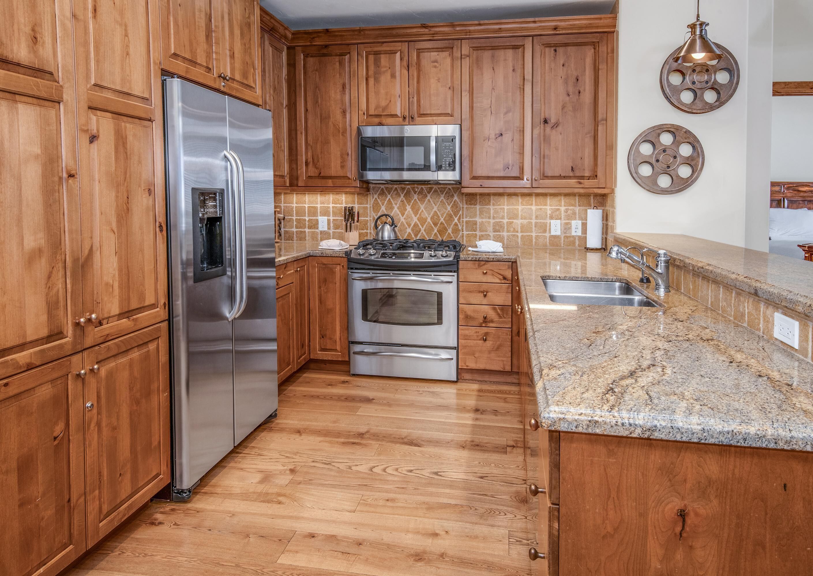 A kitchen with wooden cabinets, stainless steel appliances, a granite countertop, and a microwave.